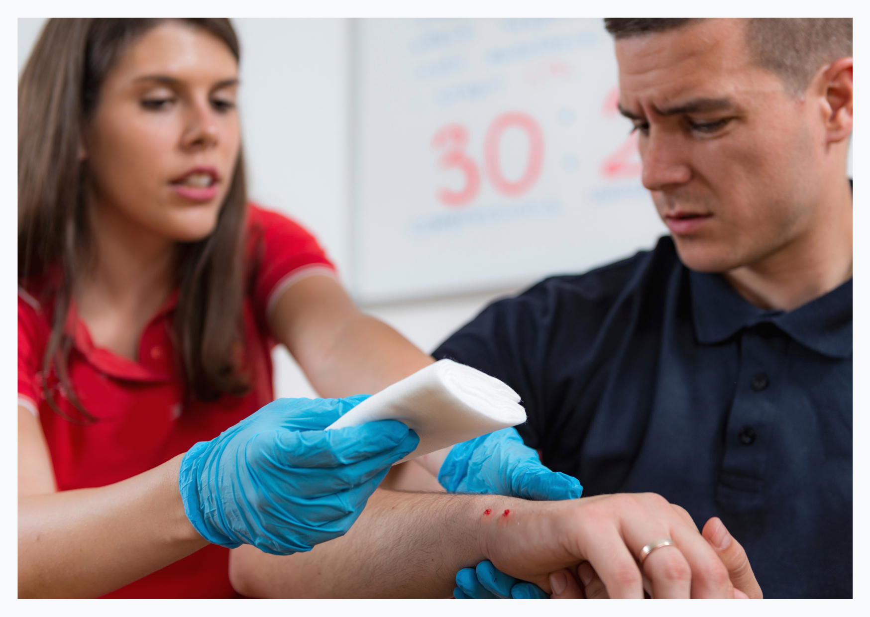 A female first aider is applying a bandage to a wound on a man's arm.